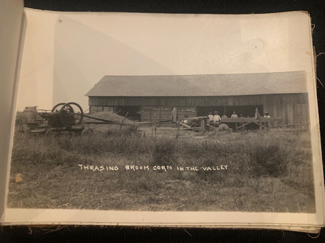 Workers and machinery thrashing broom corn outside a large barn in the Rio Grande Valley.